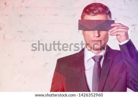 Mature businessman covering eyes with paper against white brick wall at office