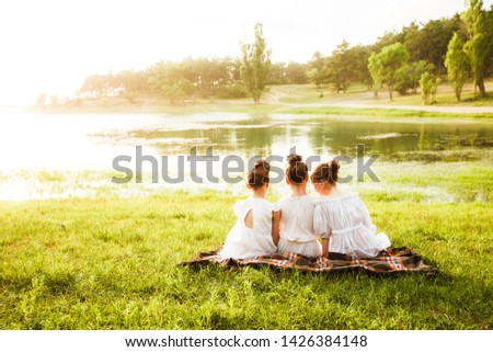 Three girls in white dresses walk in nature in the summer. Children's pastime during the summer holidays.