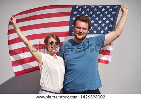 Young smiling caucasian couple of americans holding USA flag behind