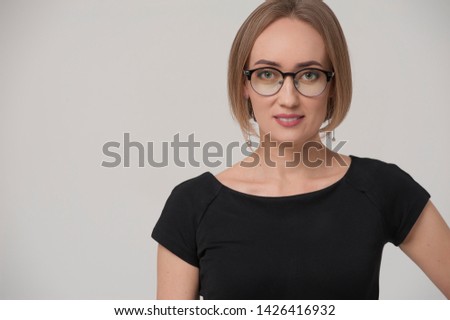 Smiling charming young businesswoman wearing formal suit and stylish glasses posing on grey background.
