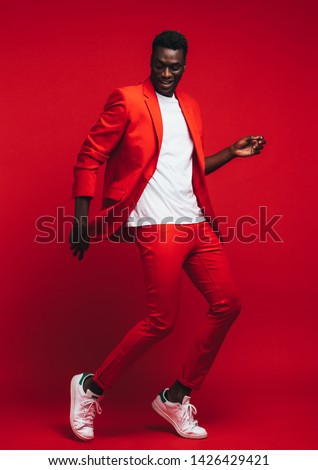 Full length od handsome young african man dancing on red background. Man in stylish red outfit showing some dance moves.