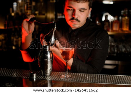 Professional bartender spraying from the diffuser on the delicious cocktail in the glass on the bar counter in the dark blurred background