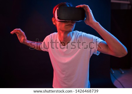 Looking at details. Young man using virtual reality glasses in the dark room with neon lighting.