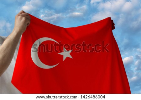 beautiful national flag of the country of Turkey in male hands against the blue sky with clouds