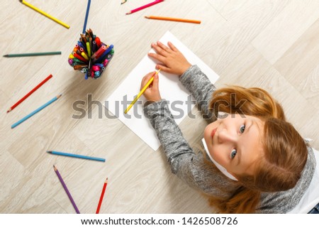 Top view of little girl painting, looking at camera and sitting on the floor in her room at home.