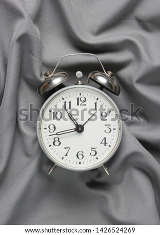 Retro alarm clock on a gray silk bedspread. Top view