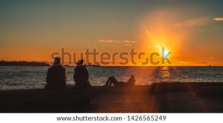 Friends sitting on a log while watching the sun set across the ocean