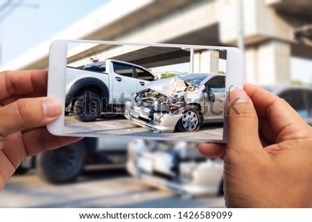 Car insurance agents take pictures of car accident-damaged vehicles with a smartphone as a proof of insurance claim.