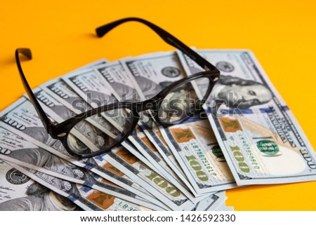 Hundred USA dollars with glasses on it, a lot of American cash money, on orange background