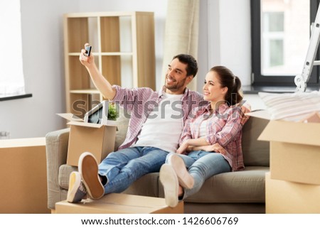 moving, repair and real estate concept - smiling couple taking selfie by smartphone at new home