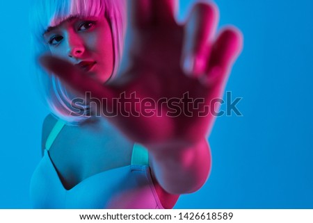Crop futuristic lady in bra looking at camera and interacting with camera against blue background