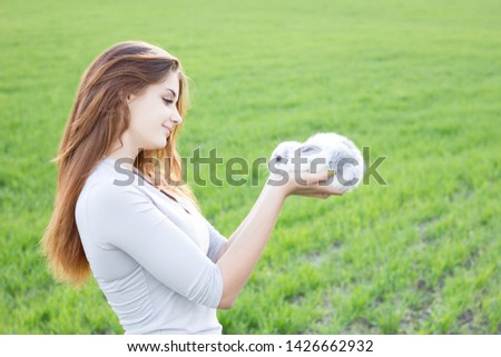 Girl holding a rabbit while on a green meadow. Young smiling girl holding a little fluffy white rabbit. Friendship with Easter Bunny. Spring photo with beautiful young girl with her Bunny