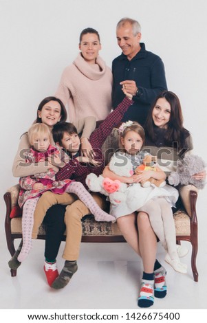 group of people on a white background: adults and children with toys sitting on the same couch