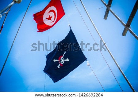 Pirate flag and the flag of Tunisia on the mast of a sailboat in the Mediterranean sea.