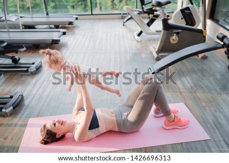 Young sporty mother and baby girl do exercises together in the gym. Parent and child healthy development, fitness and relaxation. Healthy lifestyle concept.