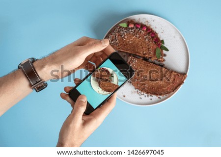 men's hands make a photo of a chocolate cake on your smartphone on a blue background. Blogging and food photos.