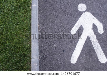 White pedestrian figure walking towards the edge on the road, bordering on a garden. Conceptual idea of person and environment, so that man meets nature, copy space.