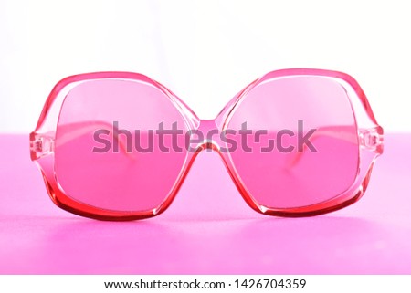 Pink perspex 70's style sunglasses against pink and white background  Royalty-Free Stock Photo #1426704359