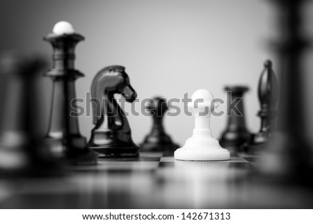 white pawn surrounded by black chess pieces on a chess board Royalty-Free Stock Photo #142671313