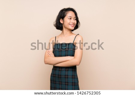 Asian young woman over isolated yellow wall with arms crossed and happy