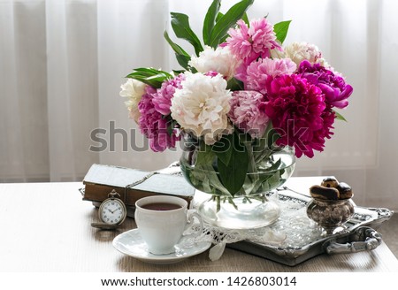 on the table a bouquet of multicolored peonies, eclairs in a vase, a cup of tea, a book and a pocket watch - tea time