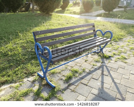 Wooden bench with metal legs in the park against concrete plates and green grass