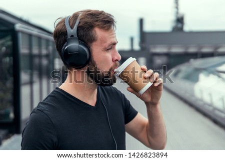 Young beard handsome man drinking coffee and listening music in headphones, posing in the street, outdoor hipster portrait,glass talking on the phone, wearing sunglasses works in company, USA,hipster 
