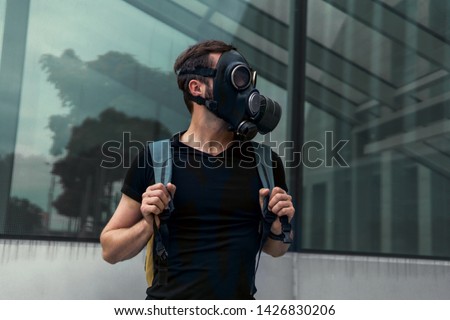 Young man in a chemical gas mask posing on the street, Man wearing gas mask and headphones making rock sign, concept business dangerous for the environment or for society, backpack, hipster, city Royalty-Free Stock Photo #1426830206