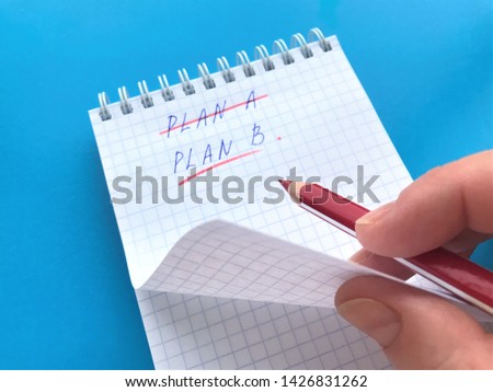 The hand holds a red pencil over the Notepad in a cell where crossed out with a red pencil Plan A, underlined Plan B and turns the page. All on a bright blue background