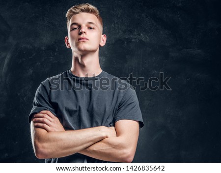 Young arrogant male is looking to the camera crossed his hands over dark background. Royalty-Free Stock Photo #1426835642