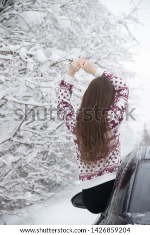 The girl in the winter outside the city. The girl sits on the car in the winter. Machine and snow trees. Winter.