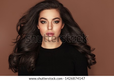 Brunette haired Woman Portrait with brown eyes and Healthy Long Shiny Wavy hairstyle. Volume shampoo. Black Curly permed Hair and bright makeup.  Beauty salon and haircare concept. Royalty-Free Stock Photo #1426874147