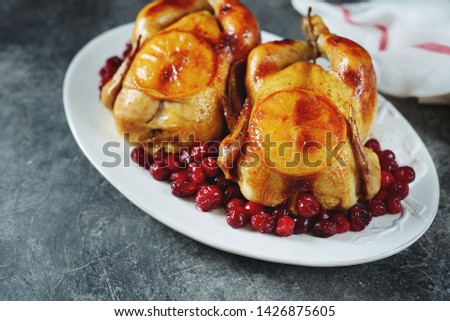 Two whole roasted chicken with cranberries and orange slices.