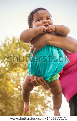 A happy little baby girl is being swung in the air by mom who is supporting her hefty weight in the background.