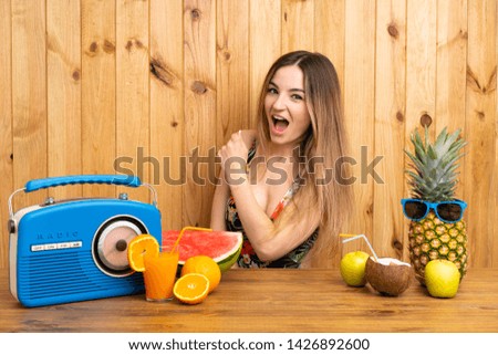 Young woman in swimsuit with lots of fruits celebrating a victory