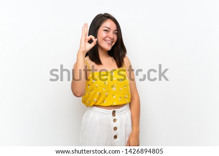 Young Mexican woman over isolated wall showing ok sign with fingers