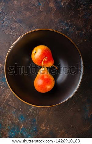 Fresh red-yellow pears on a plate on brown table, top view
