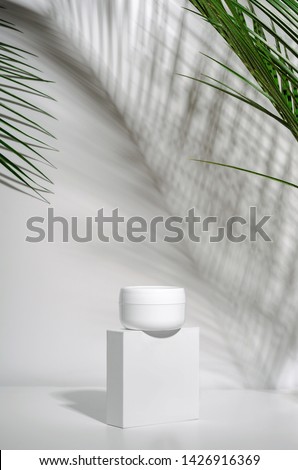 White jar of cream on a stand on a white background with tropical palm leaves and their shadow. Stylish look of the product, mock up, identity. Royalty-Free Stock Photo #1426916369