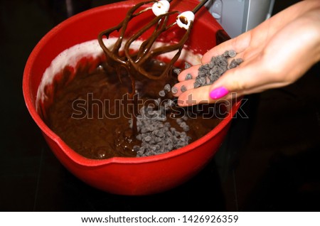 the process of making chocolate brownie cake. the girl adds with the palm of a new batch of chocolate for whipping with a mixer.