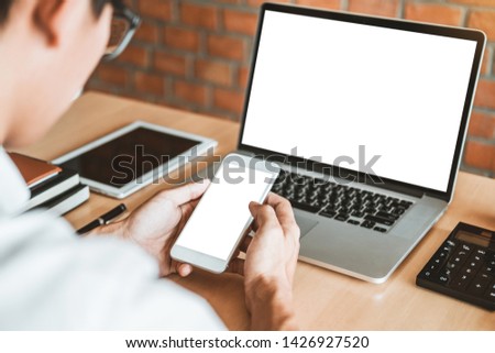 Businesss man using laptop and Mobile Phone with blank screen in the office.