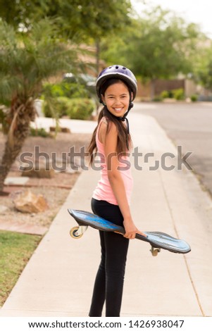 Young girl playing outside with a skateboard.