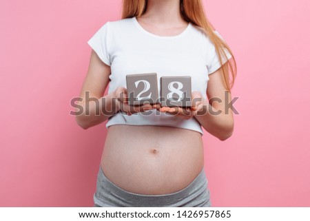 Macro image of a pregnant woman holding wooden cubes near the belly, 9 months of pregnancy on a pink background