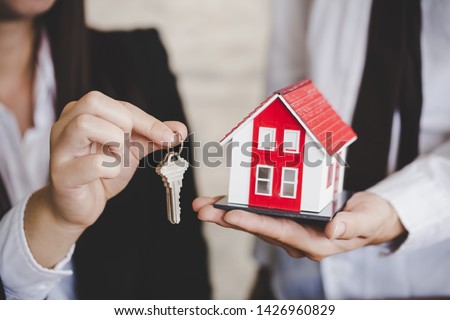 Young lady taking keys from female real estate agent during meeting after signing rental lease contract or sale purchase agreement.  Royalty-Free Stock Photo #1426960829