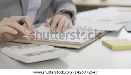 female businesswoman in suit hand using calculator plan to write and sign check book with graph data paper on desk at office. Paycheck concept. secretary assistant accounting financial in company