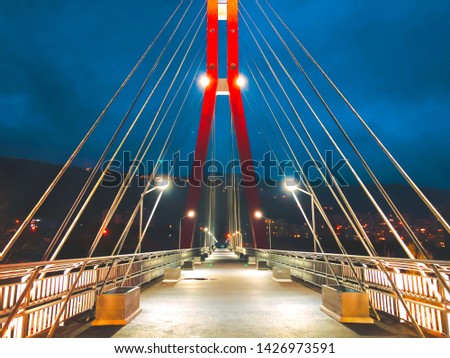 Sidewalk area going through a cable-stayed bridge with big steel cables, closeup at night time in bright lights.