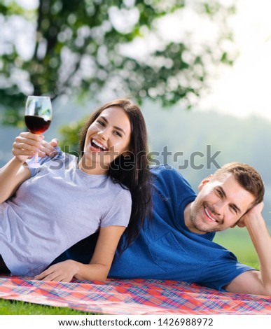 Picture of young couple in love, lying together on a picnic blanket with wine, outdoors
