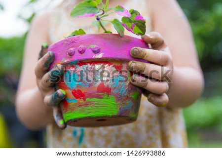 Small child holds a brightly painted pot with a plant in it with grubby hands  Royalty-Free Stock Photo #1426993886