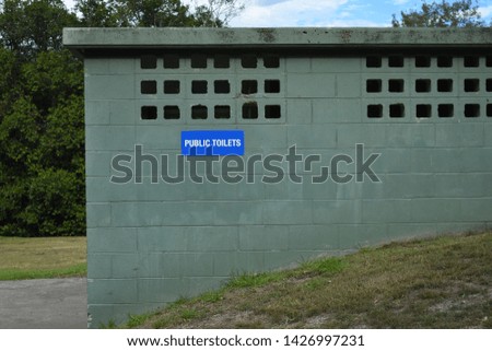 Green public toilet building with blue sign and grass foreground 