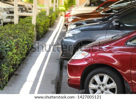 Closeup of front side of red car with  other cars parking in parking lot in bright sunny day. The mean of simply transportation in modern world.
