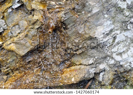 Surface of rocks wall with water flowing.  Clear water flows from the rock, for convenience, people in Tbilisi installed a plastic bottle for the convenience of water intake.